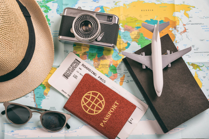 Premium travel essentials flat lay with passport, boarding pass, airplane model, and camera on world map — international vacation planning concept by EswarTours